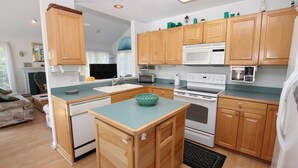 A compact kitchen with wooden cabinets, a built-in microwave, a stove, and a sink. - Oceanside, Community Pool, Community Amenities, 677, Windswept II (Corolla)
