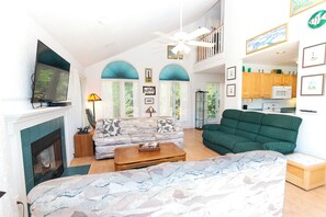A spacious living area with a fireplace, a sofa, a coffee table, and a television. - Oceanside, Community Pool, Community Amenities, 677, Windswept II (Corolla)