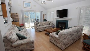 A living room with two patterned sofas, a wooden coffee table, and a television above a fireplace. - Oceanside, Community Pool, Community Amenities, 677, Windswept II (Corolla)