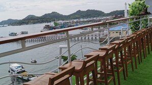 Um bar à beira-mar com bancos de madeira e vista para barcos e um cais.