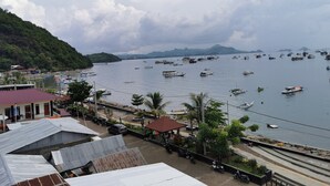 Uma vila costeira com barcos atracados na orla, uma estrada com motocicletas estacionadas e edifícios com telhados metálicos.