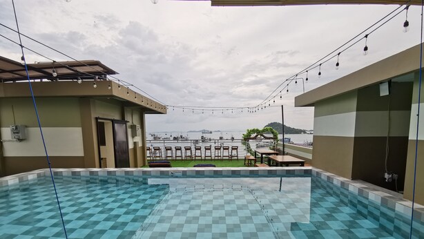 Piscina ao ar livre com azulejos quadriculados, vista de barcos na água e área de estar com mesas e cadeiras.