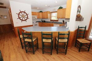 Una cocina con armarios de madera, una isla central con taburetes de bar y un adorno de timón de barco en la pared.