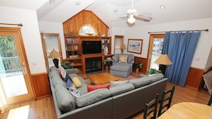 A cozy living room with a large gray sectional sofa, a wooden entertainment center, and a fireplace. - Oceanside, Private Pool, Hot Tub, Sun Decks, WC1077, Seaside Manor (Corolla)