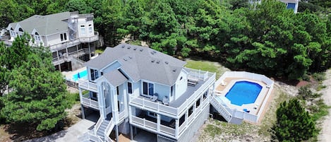 A multi-story house with a pool and a deck, surrounded by trees.