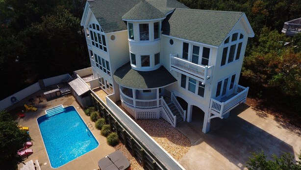 A large, multi-story house with a swimming pool, multiple balconies, and a covered deck area.
