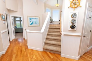 A staircase with carpeted steps leading to a landing, a framed picture on the wall, and a ship's wheel decoration.