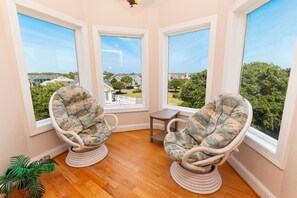Quarto com duas cadeiras de vime voltadas para uma janela de canto com vista para um bairro residencial.