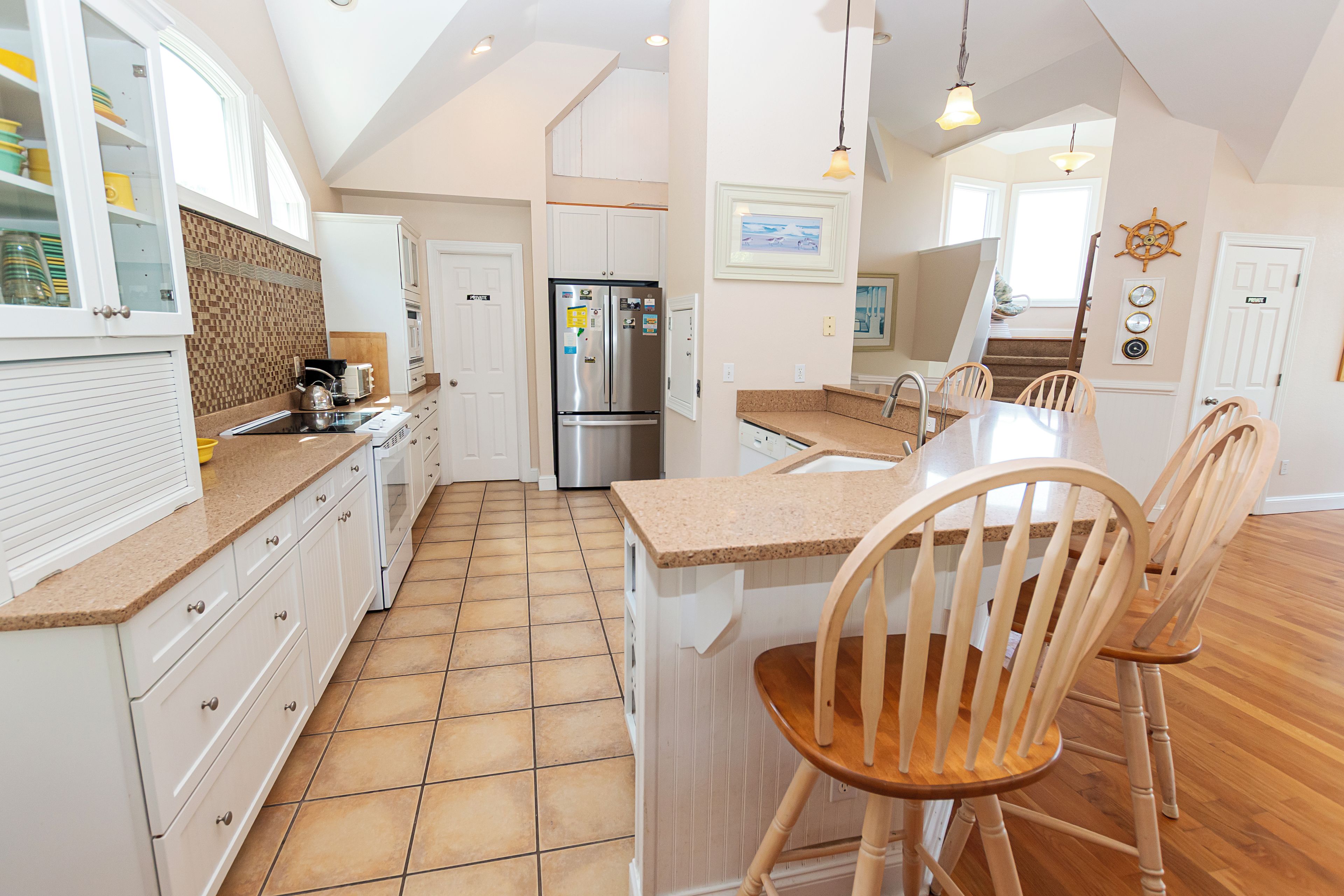A modern kitchen with white cabinetry, a stainless steel refrigerator, and a wooden dining table with chairs.