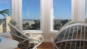 A room with two wicker chairs facing a bay window overlooking a residential area.