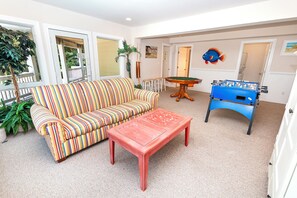 A living room with a striped sofa, a red coffee table, a foosball table, and a pool table.