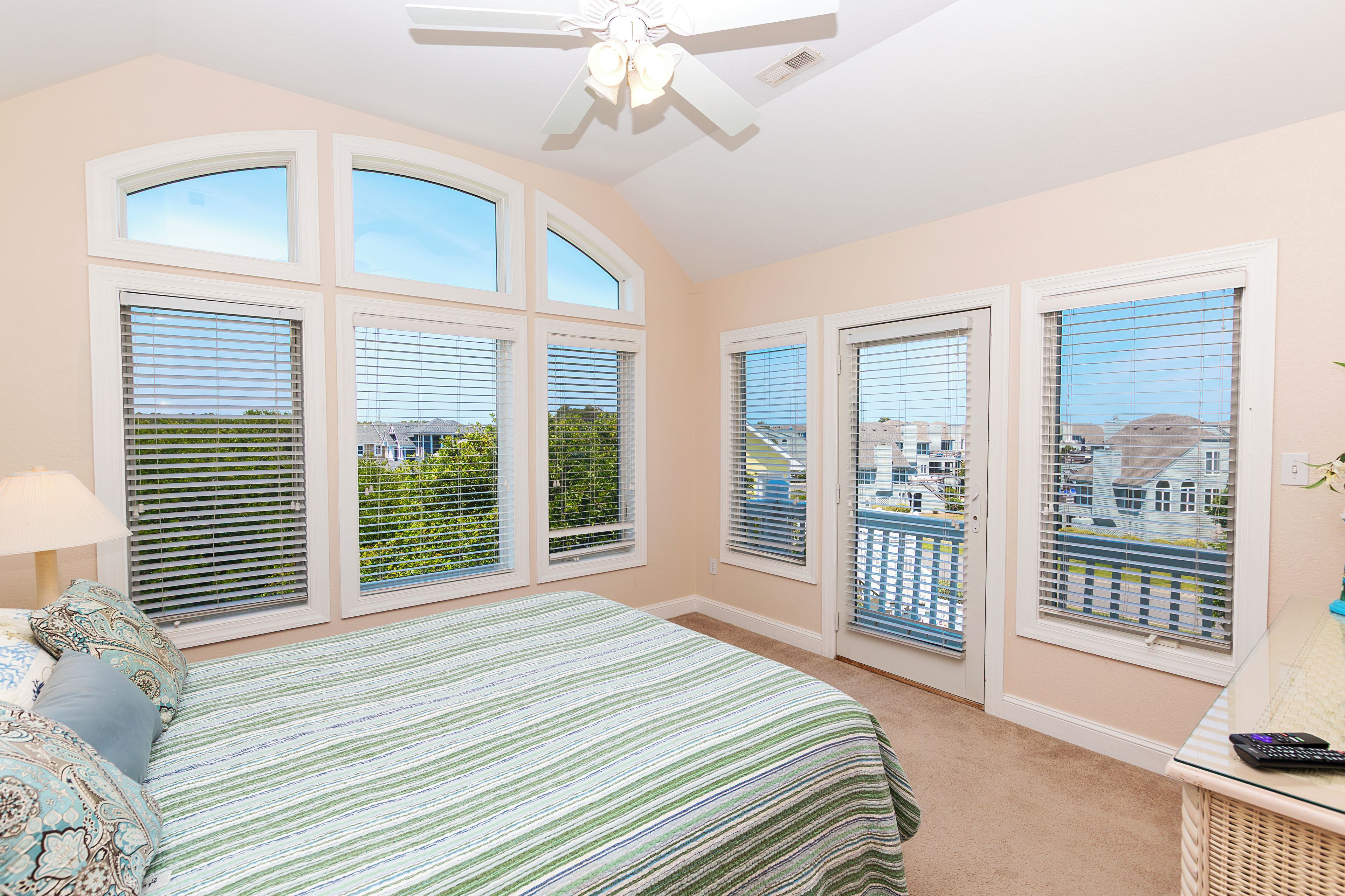 A bedroom with a bed, a ceiling fan, and large windows with blinds.