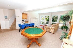 A spacious living room with a foosball table, a sofa, and a view of a garden through large windows. - Oceanside, Community Amenities, Prv Pool, Rec Rm, 5, Carolina on my Mind (Corolla)