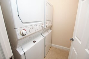 A laundry room with a stacked washer and dryer, control knobs, and a door. - Oceanside, Community Amenities, Prv Pool, Rec Rm, 5, Carolina on my Mind (Corolla)