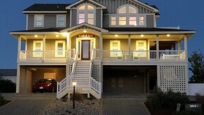 A two-story house with a covered front porch, a garage, and a car parked in the driveway. - Oceanside, Priv Pool, ELEV, Hot Tub, Keyless entry, BH3, Knot 4 Sail (Corolla)