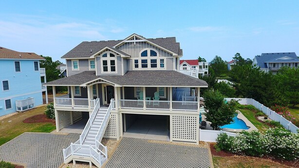 A large, two-story house with a covered front porch, a small staircase leading to the entrance, and a swimming pool in the backyard. - Oceanside, Priv Pool, ELEV, Hot Tub, Keyless entry, BH3, Knot 4 Sail (Corolla)
