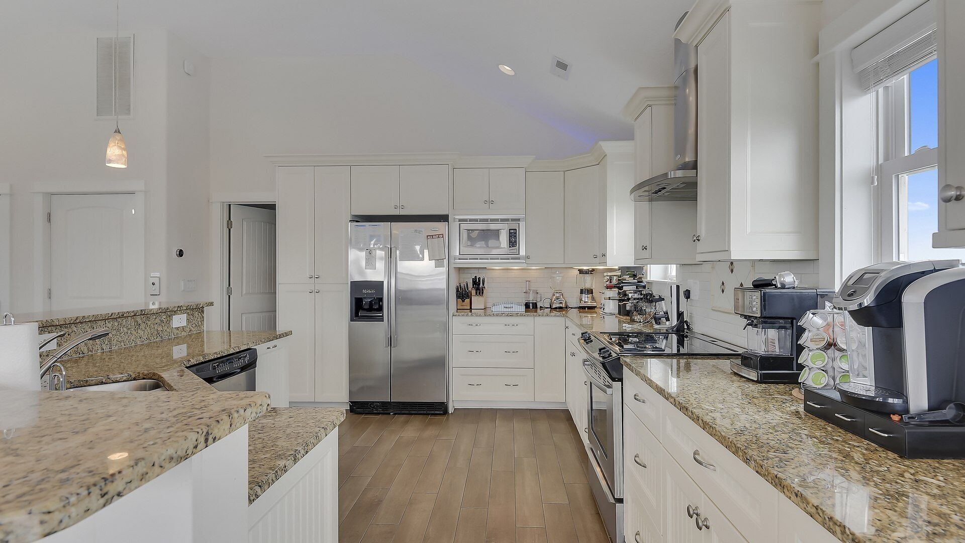 A modern kitchen with white cabinetry, granite countertops, stainless steel appliances, and a coffee machine.