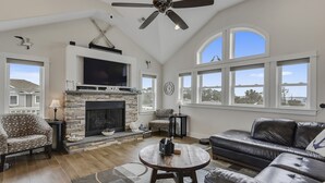 A spacious living room with a fireplace, comfortable seating, and large windows offering views of the outdoors. - Oceanside, Priv Pool, ELEV, Hot Tub, Keyless entry, BH3, Knot 4 Sail (Corolla)