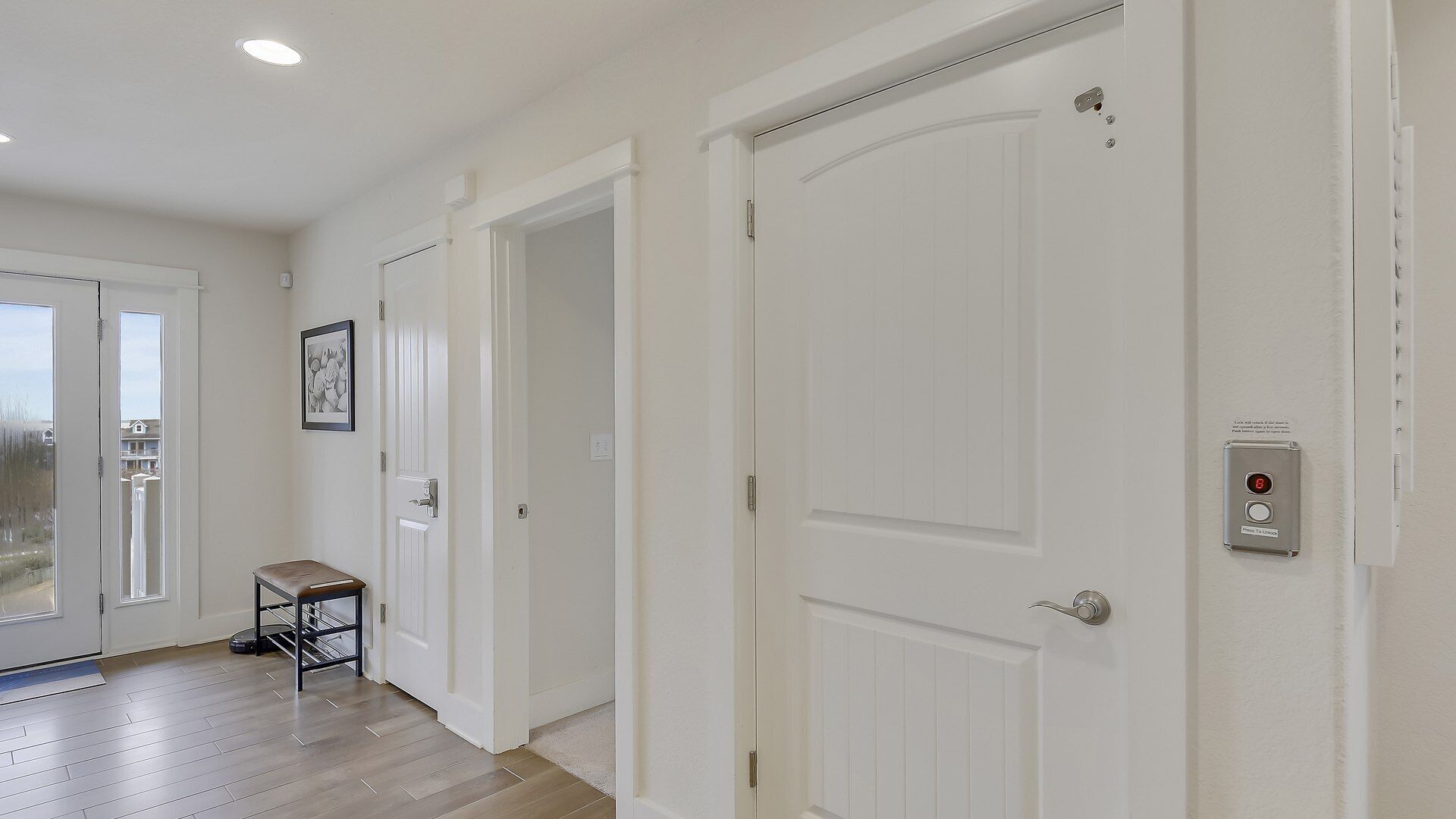 A hallway with white doors, a bench, and a security panel.