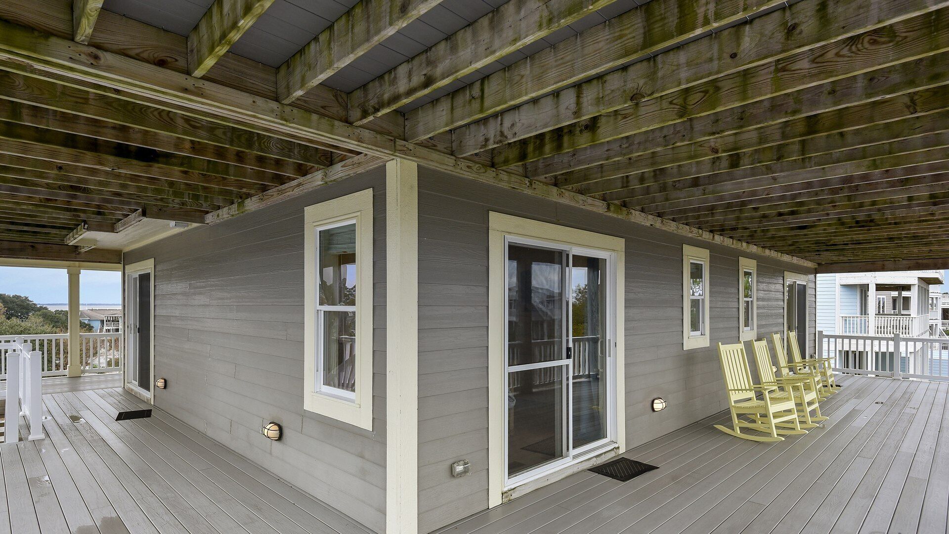 A covered deck with a wooden ceiling and grey walls, featuring a sliding glass door and two windows.