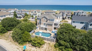 A coastal residential area with houses, a swimming pool, and a beach in the background.