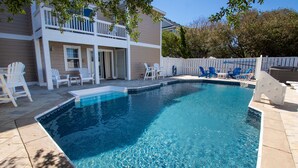 A swimming pool with a clear blue water surface, surrounded by a white fence, and adjacent to a two-story house with a balcony.
