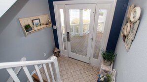 A hallway with a white railing, a door leading to an outdoor deck, and a shelf with decorative items. - Oceanside, Hot Tub, Dogs Welcome, Community Pool, BU13B, Tropical Dreams B (Corolla)