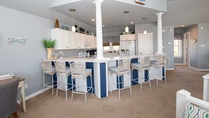A kitchen with white cabinets, a central island with bar stools, and a hanging light fixture. - Oceanside, Hot Tub, Dogs Welcome, Community Pool, BU13B, Tropical Dreams B (Corolla)