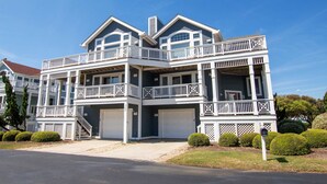 A two-story house with a balcony, a garage, and a well-maintained lawn. - Oceanside, Hot Tub, Dogs Welcome, Community Pool, BU13B, Tropical Dreams B (Corolla)