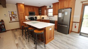 A kitchen with wooden cabinets, a stainless steel refrigerator, a microwave, and a bar stool area. - Semi-Oceanfront, Close to Beach, Dogs Welcome, SA8, Berry (Duck)
