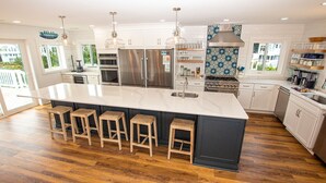 A modern kitchen with a large island, stainless steel appliances, and wooden stools. - Oceanside, 7 BRs, Private Pool, Den, Rec Rm, 350 ft to Beach access, PI54, Fore Sea Suns (Corolla)