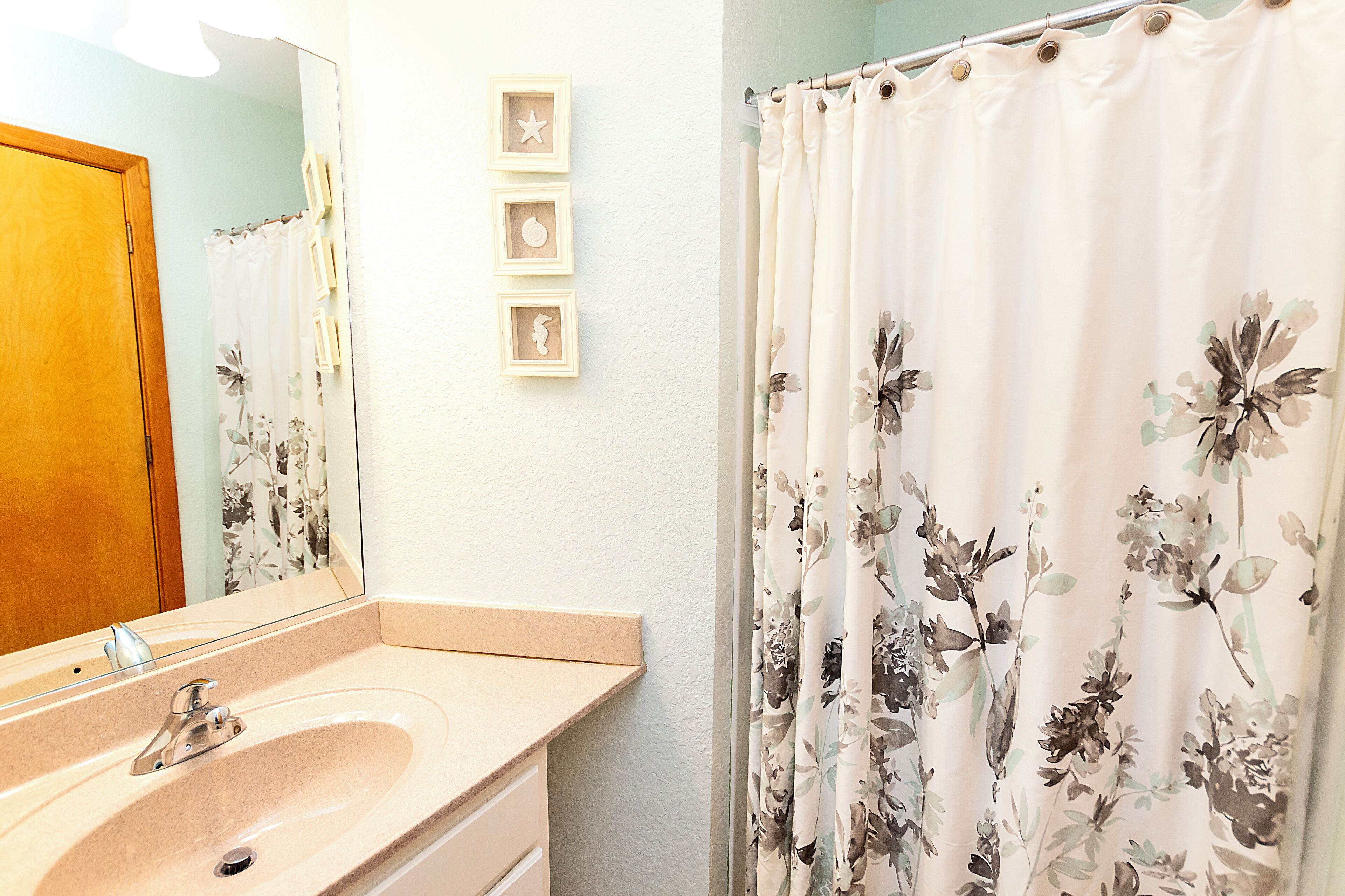 A bathroom with a sink, mirror, and floral shower curtain.