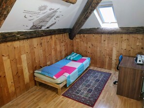 A small, cozy room with wooden walls, a single bed, a desk, and a window.