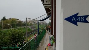 A corridor with a green fence, a bench, and a directional sign pointing left. - A46 Foresteria Lombarda (Monza)