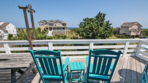 A wooden deck with turquoise chairs and a small table, overlooking a residential area with houses and a clear sky.