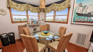 A dining area with a glass table surrounded by wicker chairs, a decorative lamp, and a window with a floral valance.