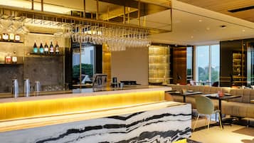 A modern bar area with a marble countertop, wine glasses, and bottles. There is a seating area with sofas and a view of the outdoors.