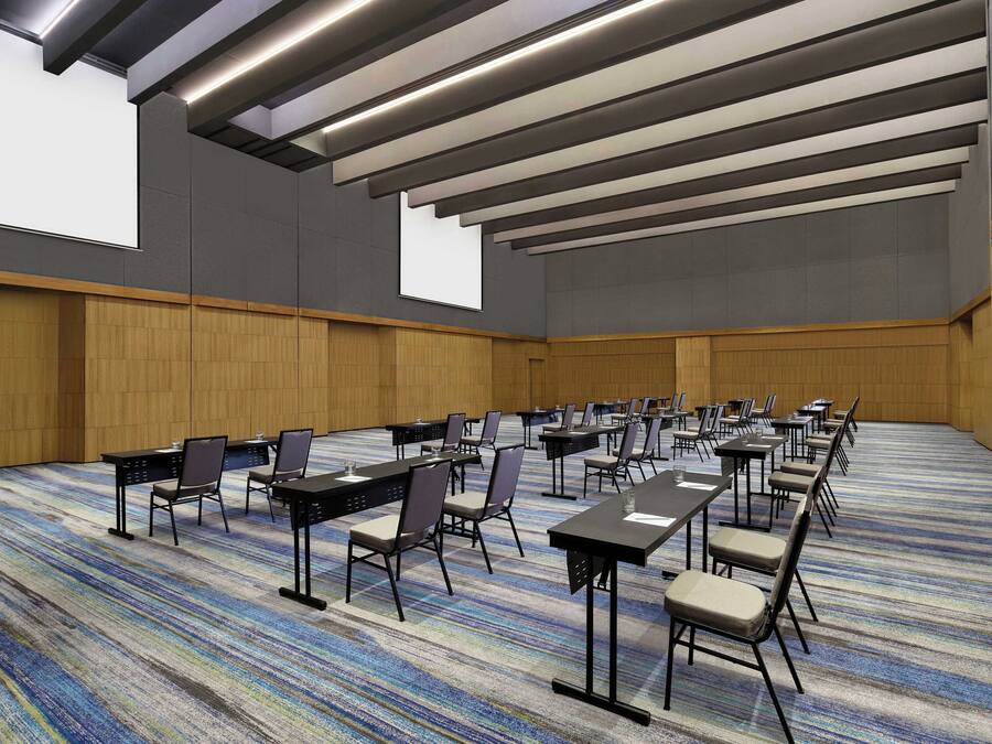 Un salón de conferencias con varias mesas y sillas, una alfombra estampada y un techo alto con iluminación empotrada.