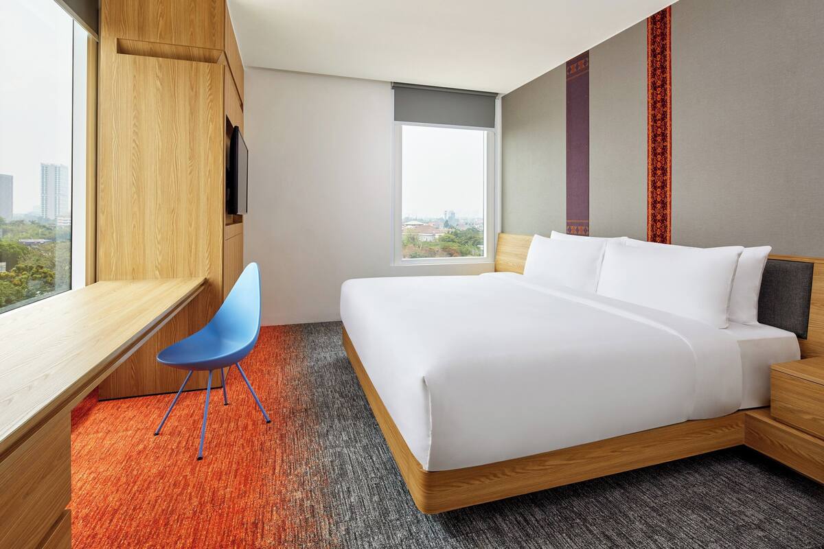 A modern hotel room with a large bed, a desk, and a chair.