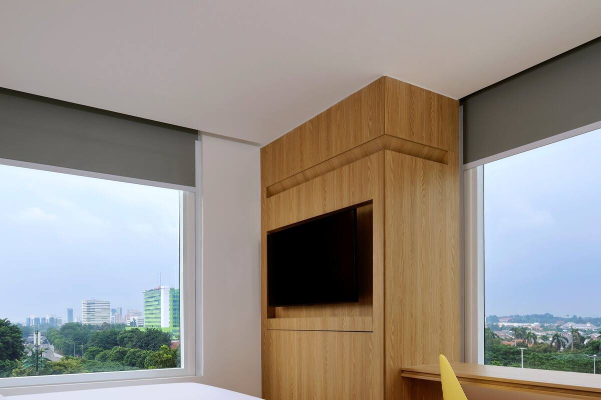 A modern hotel room with large windows, a flat-screen TV, and a wooden accent wall.