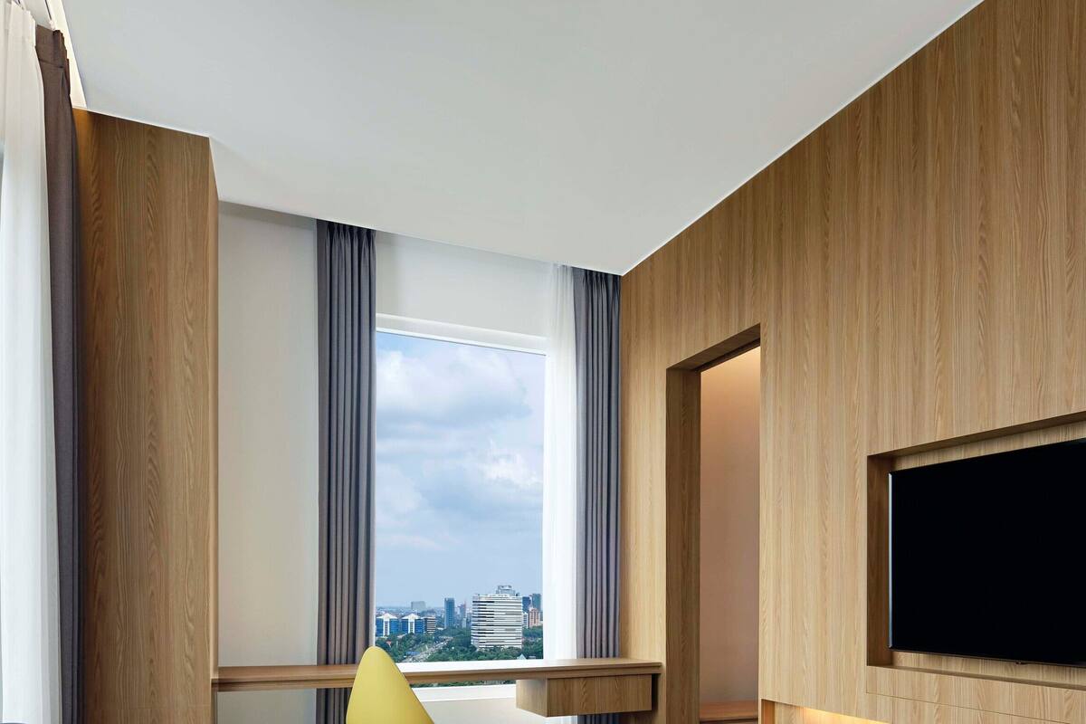 A modern hotel room with a large window, a flat-screen TV mounted on the wall, and a wooden panel design.