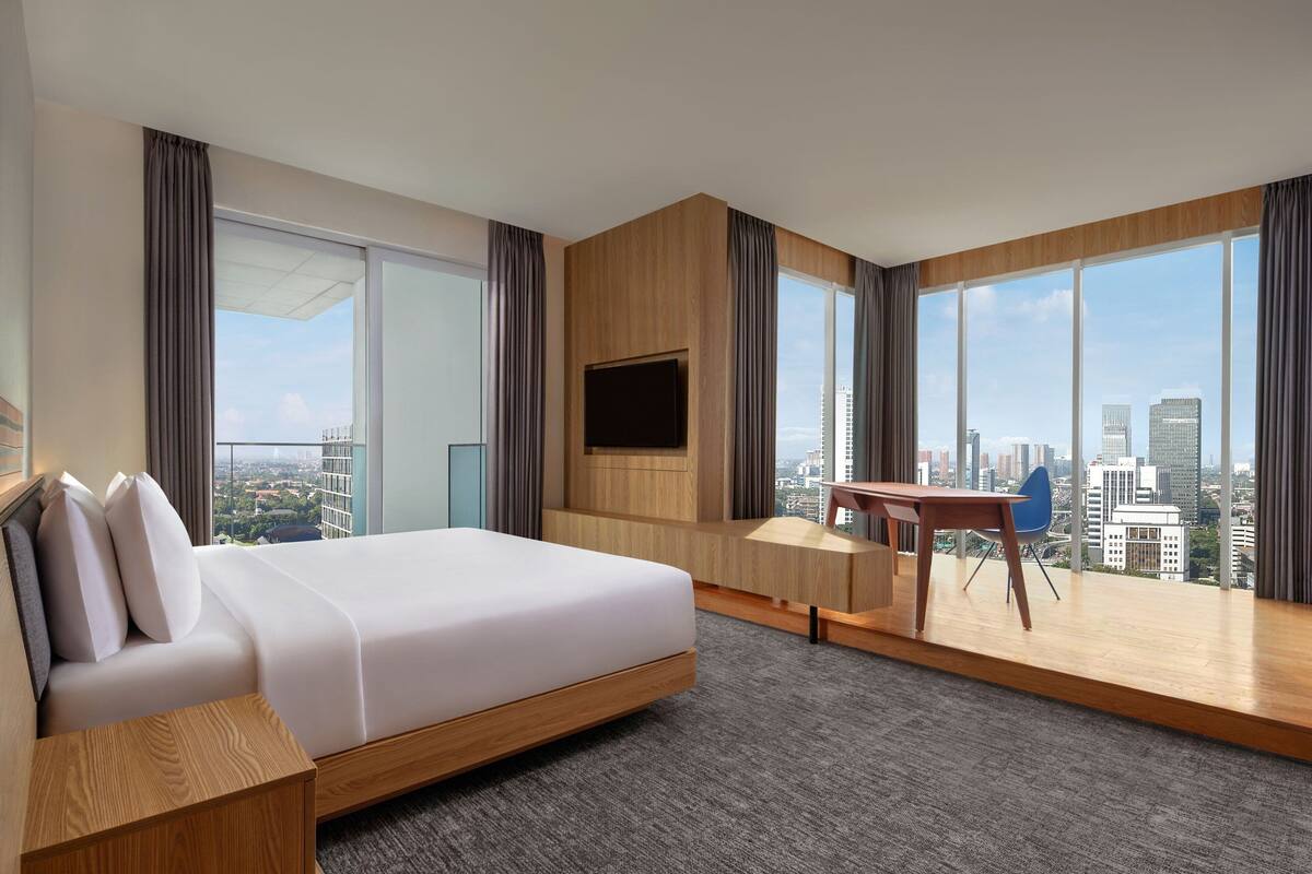 A modern hotel room with a large bed, a desk, and a TV.