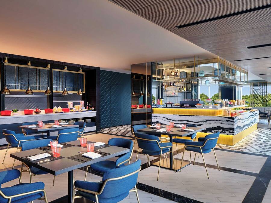 A modern restaurant with blue and yellow seating, a bar area, and a view of greenery.