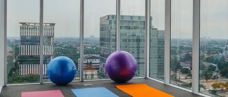Habitación en un edificio alto con vista a la ciudad, con equipo de ejercicio y colchonetas de yoga en el alféizar de la ventana.