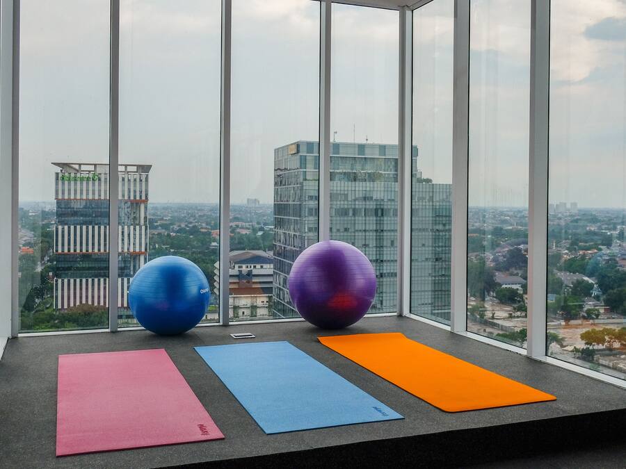 Camera in un grattacielo con vista sulla città, dotata di attrezzature per esercizi e tappetini da yoga su un davanzale.