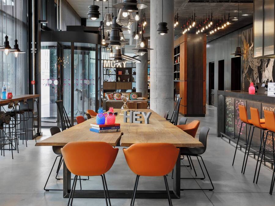 Un café moderne avec une table en bois, des chaises orange et des luminaires suspendus.