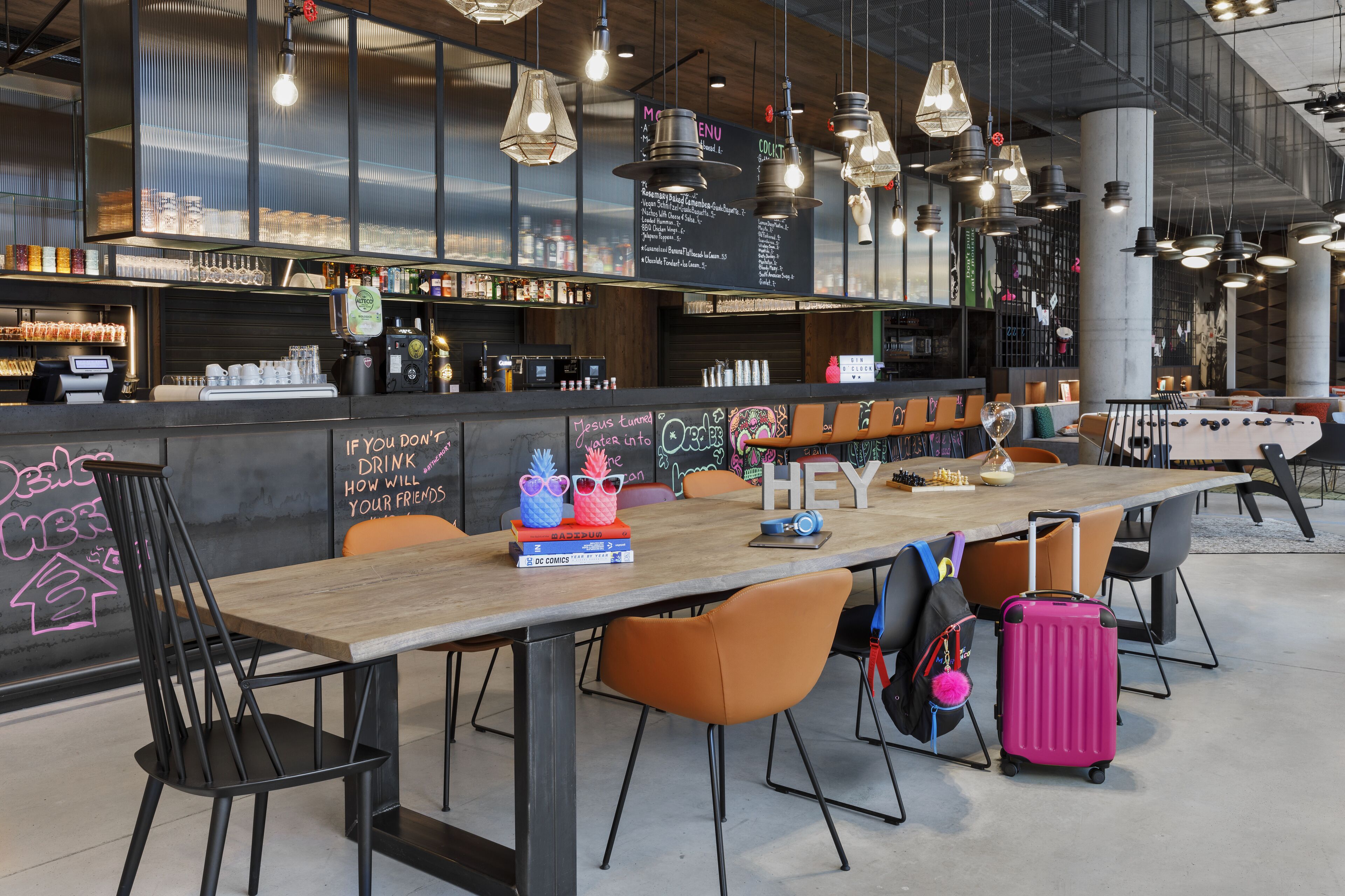 Un bar moderno con una mesa de madera, sillas anaranjadas y una maleta rosa.