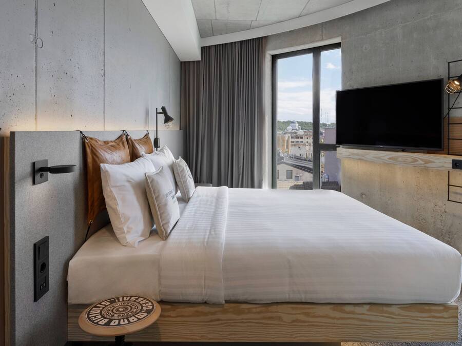 Une chambre d’hôtel moderne dotée d’un grand lit, d’une télévision à écran plat et offrant une vue sur la ville par la fenêtre.