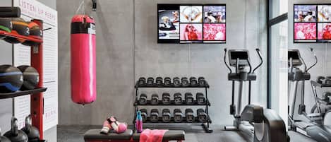 Un gimnasio con saco de boxeo, mancuernas, bancos, cintas de correr y equipo de ejercicio.