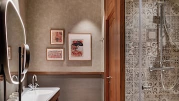 A bathroom with a modern vanity, a large mirror with lights, and a shower with decorative tiles.